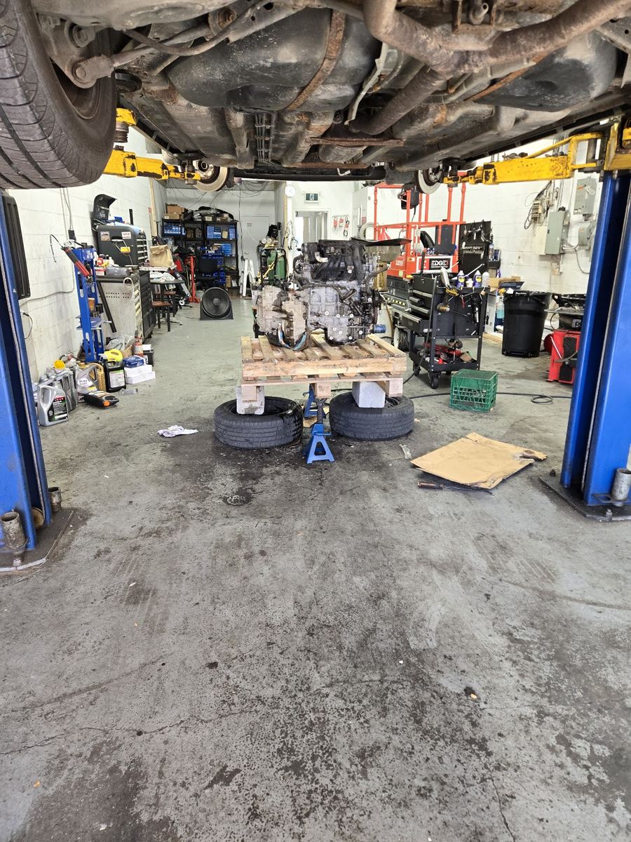 Inside the bay at Kam Auto Repair: a car on the hoist and an engine on a pallet