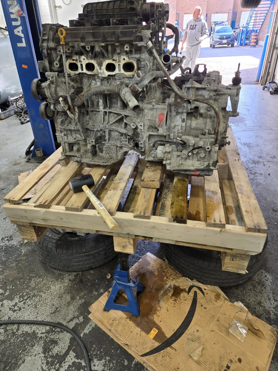 An engine and transmission removed from a car, on a pallet in the shop
