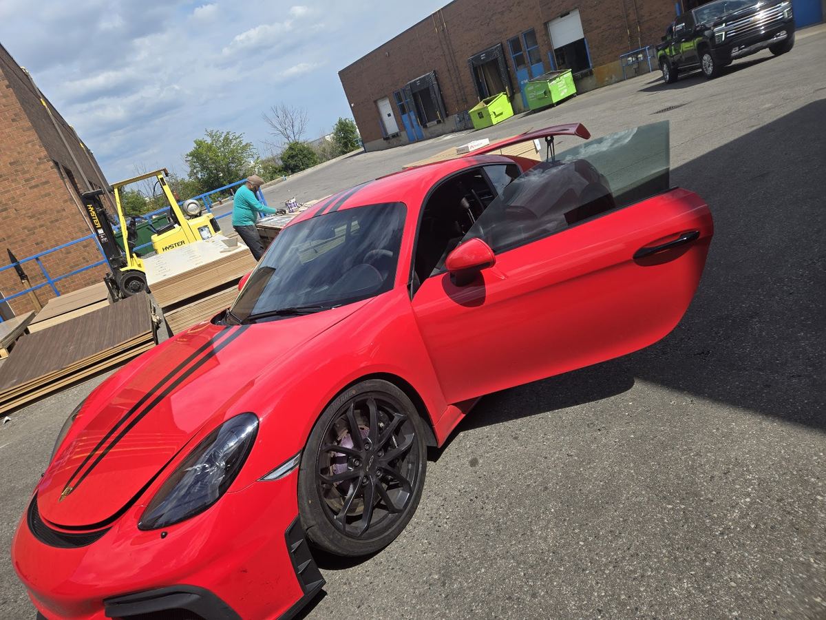 A red Porsche Cayman GT4 in front of the shop